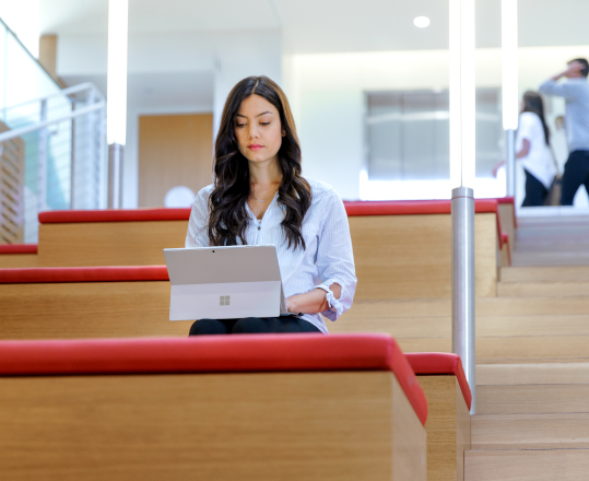A young woman sits in an empty auditorium on her computer.