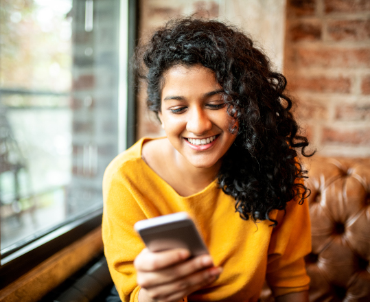 A young woman smiles as she looks at her phone.