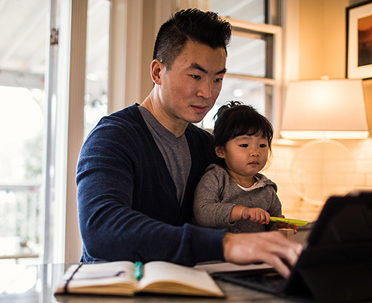 Man working on laptop with child on his lap