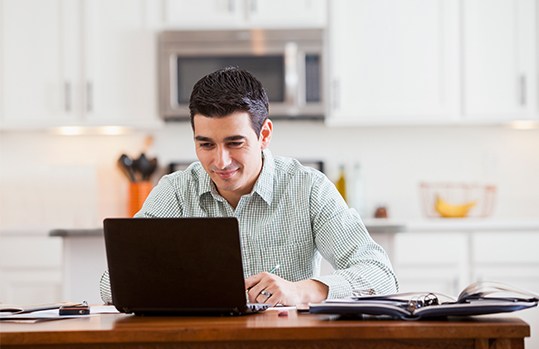 Man smiling at his laptop screen in a kitchen