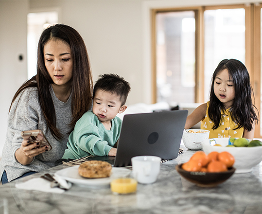 Woman multi-tasking with young children in kitchen table