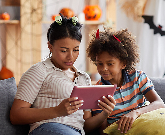 woman and son in Halloween-themed gear look at tablet on couch