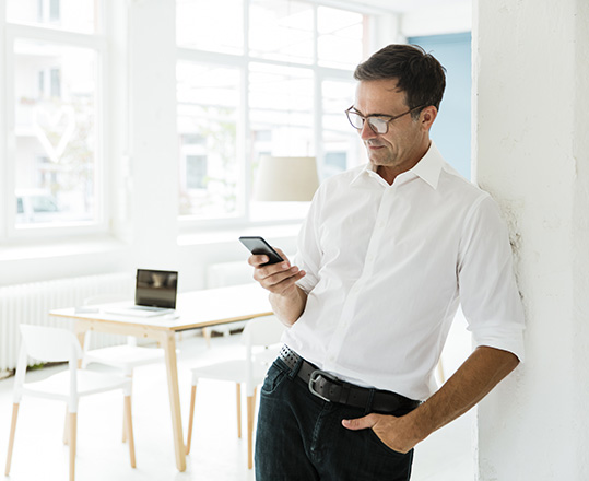 Businessman looking at smartphone in a bright office.