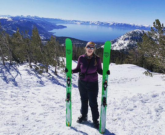 AAli Forelli posing with skis in the snowy mountains with a lake in the background