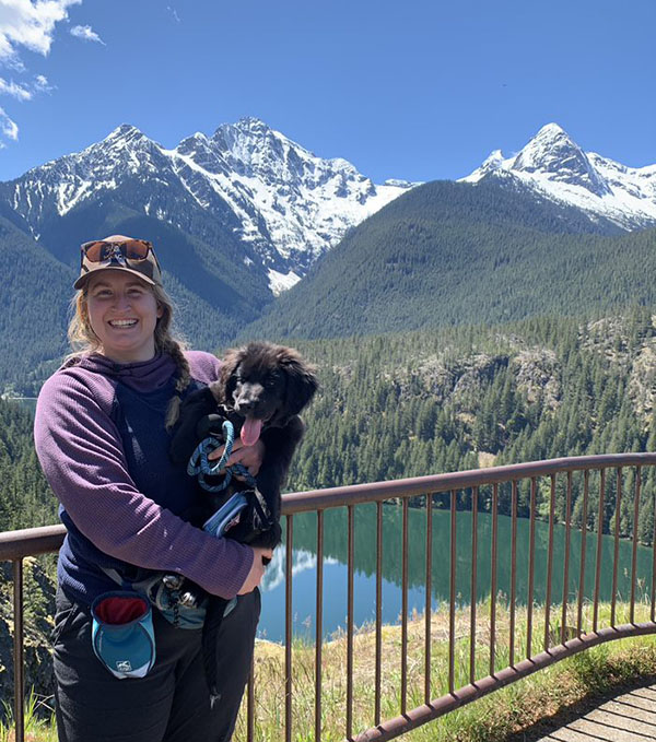 Ali Forelli standing in front of mountains with her puppy.