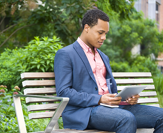 Young businessman sitting on park bench looking at digital tablet
