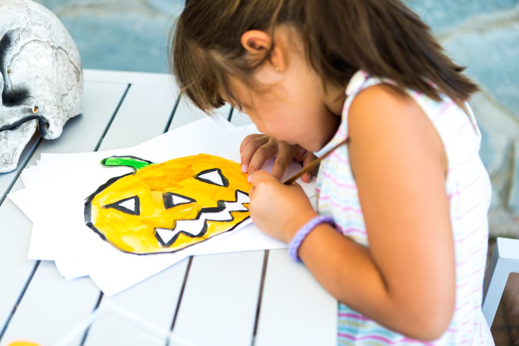 Girl coloring a pumpkin at the table.